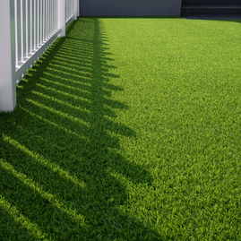 Green artificial grass residential lawn with white picket fence